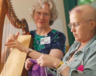 A lady plays the harp as a patient listens.