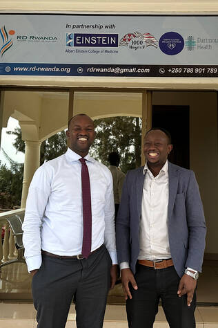 Two doctors standing in front of a building that displays RD Rwanda and Dartmouth Health logos