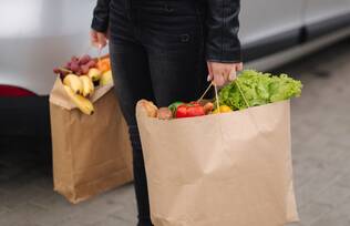 Person carrying brown paper grocery bags by the handle.