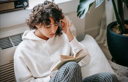girl with hand against her forehead while reading a book