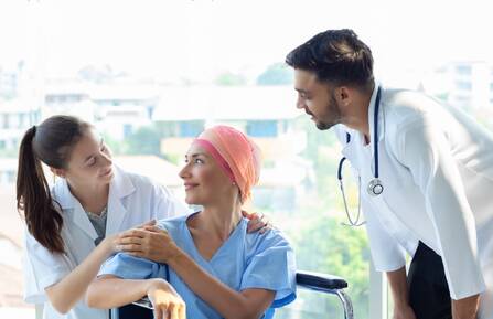 Cancer patient wearing head covering surrounded by two healthcare workers
