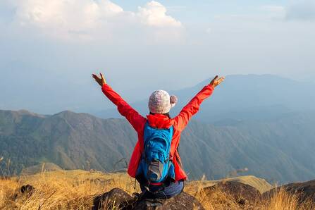 A hiker at the top of a mountain with their arms outstretched shown from behind