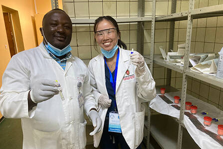 Two smiling doctors stand next to each other holding vials with liquid in them