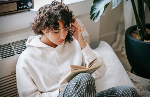 girl with hand against her forehead while reading a book