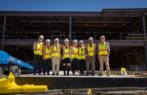 Dartmouth Cancer Center employees pose in front of construction site wearing construction vests and hard hats