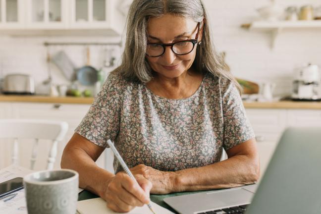Middle aged woman sitting at laptop with pen and coffee